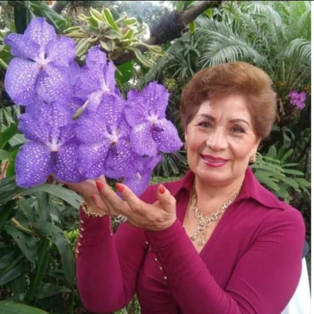Reyna Cortés Torres, sosteniendo unas orquídeas moradas.